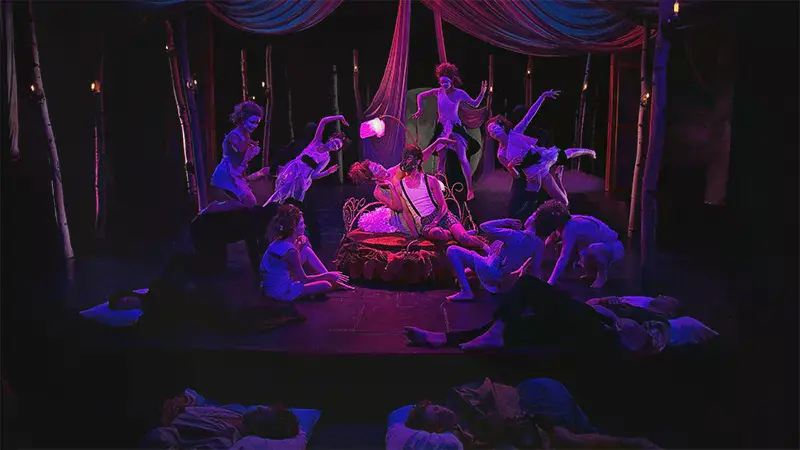 A couple on a bed with dancers surrounding them in A Midsummer Night's Dream