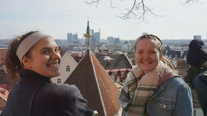Two female students take a selfie on a hill overlooking the Tallin skyline in Estonia