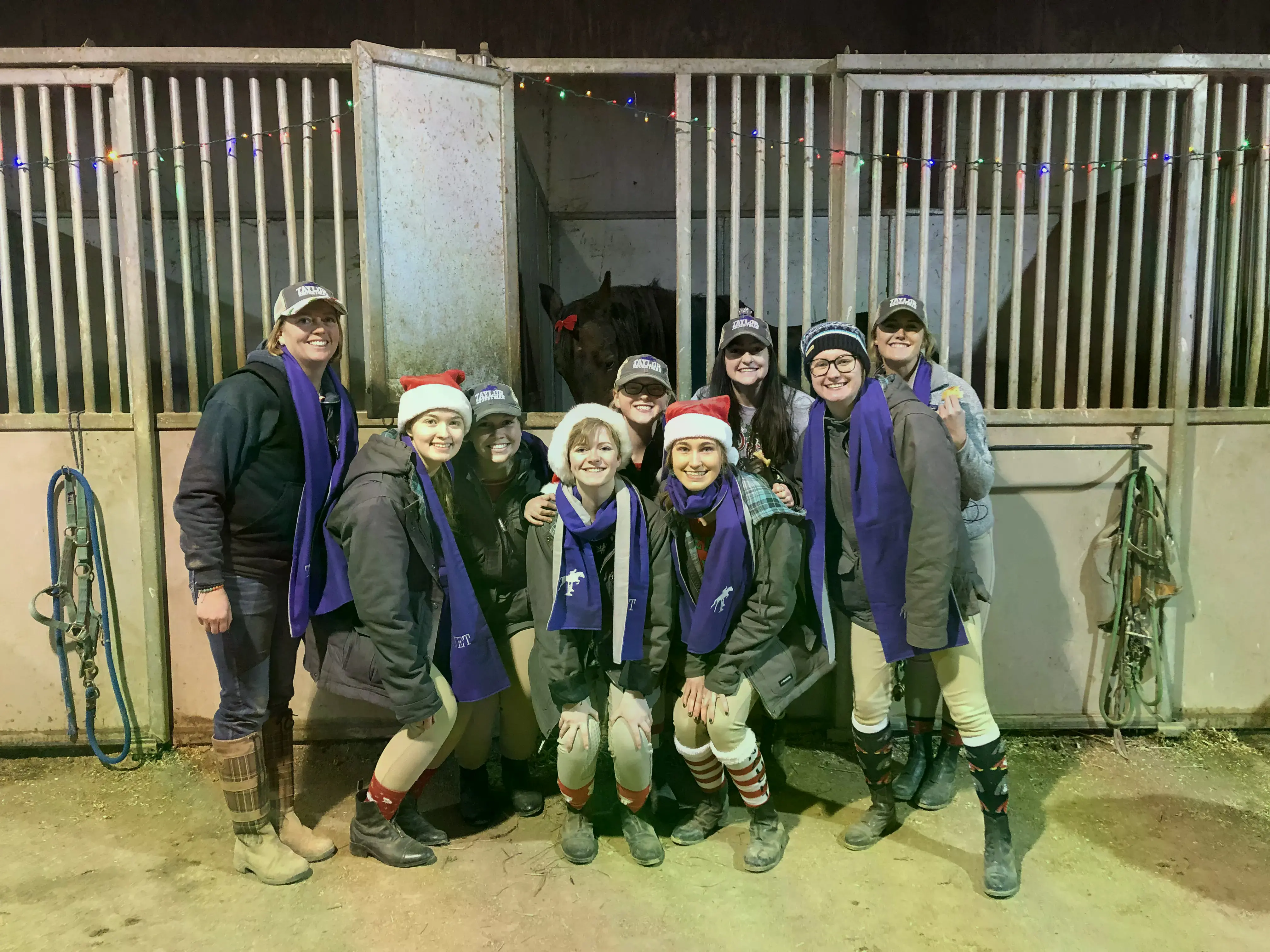 The Equestrian Team in hats and scarves in front of a stable