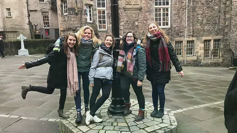 Five girls standing around a lamp post in a stone brick courtyard