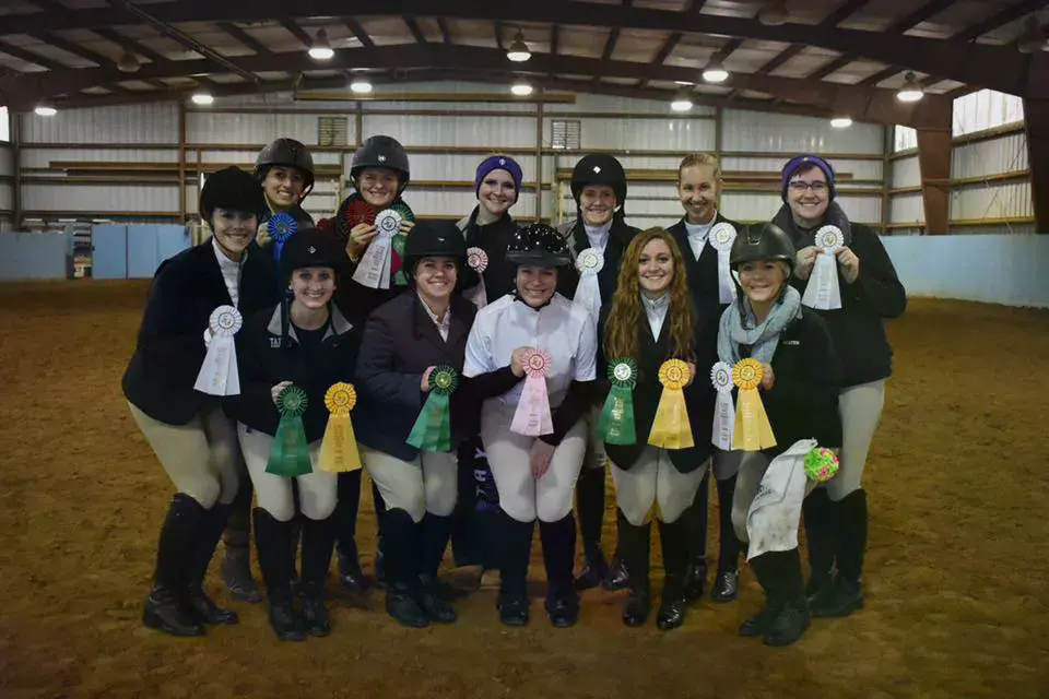 The Equestrian Team standing in an indoor arena holding their ribbons