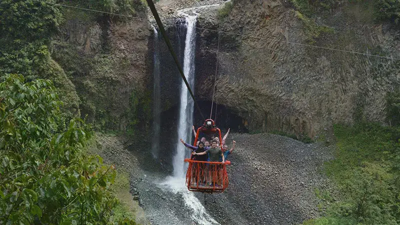 Multiple students riding in a cable car over a forest waterfall and valley