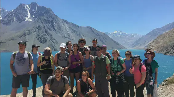 Group of Taylor students huddled for a picture in front of a river and some mountains in Chile