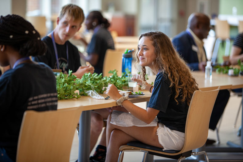 Student smiling sitting at a table with greenery at LaRita Boren Campus Center