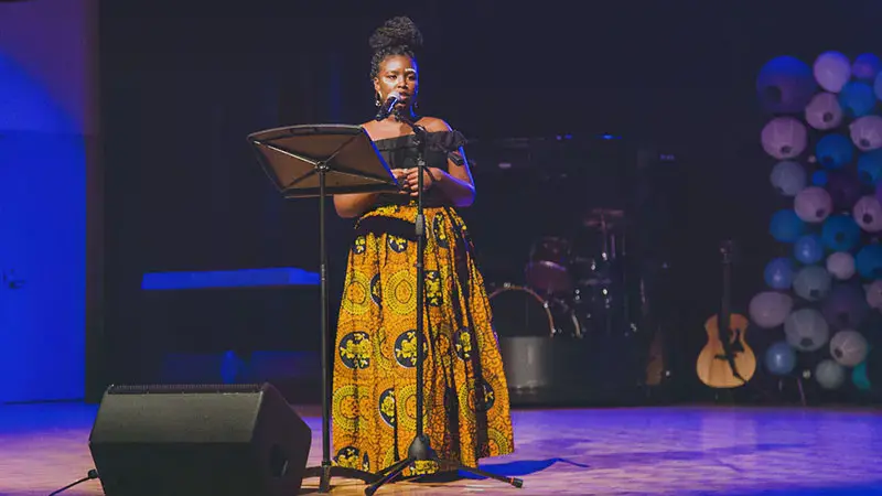 A student in a long yellow skirt reciting spoken-word poetry