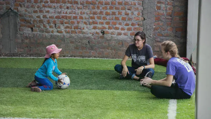 Two female students rolling a soccer ball on the ground with a girl