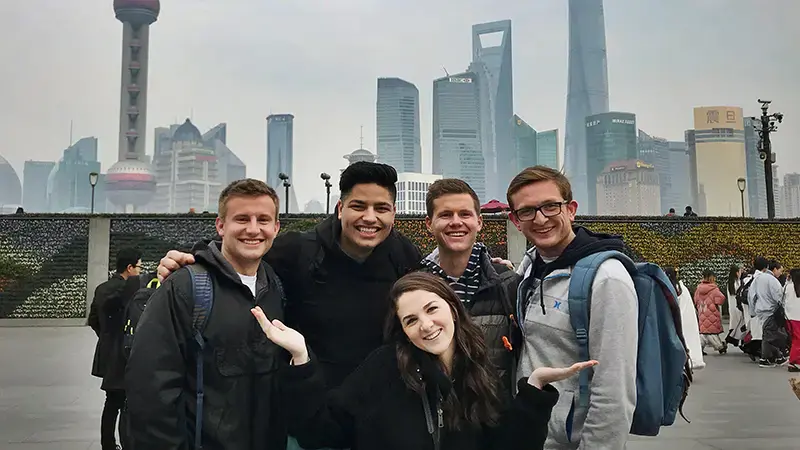 Five students posing in front of Chinese skyline