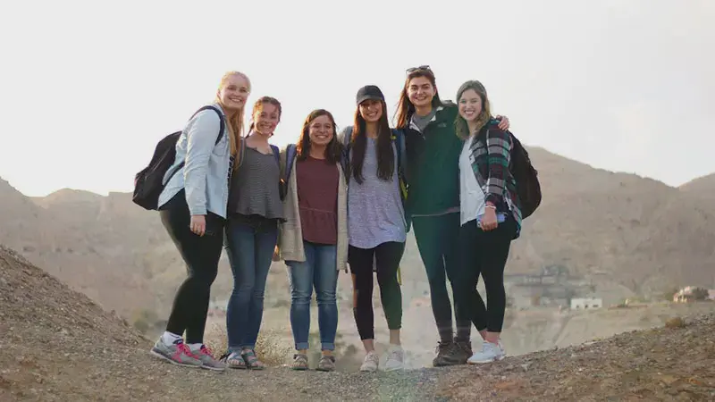 Six female students standing on a rocky desert hill overlooking a town