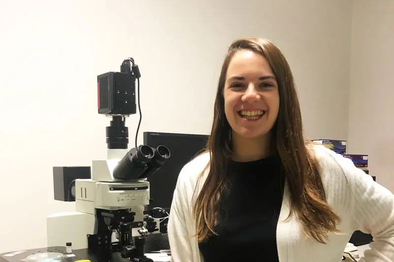 smiling female student in front of microscope