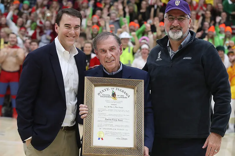 three men pose with framed award at basketball game