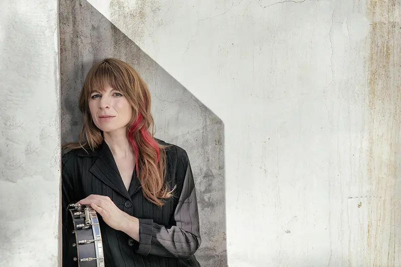 woman stands in front of wall with guitar