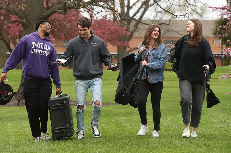 film students carrying equipmen across green grass