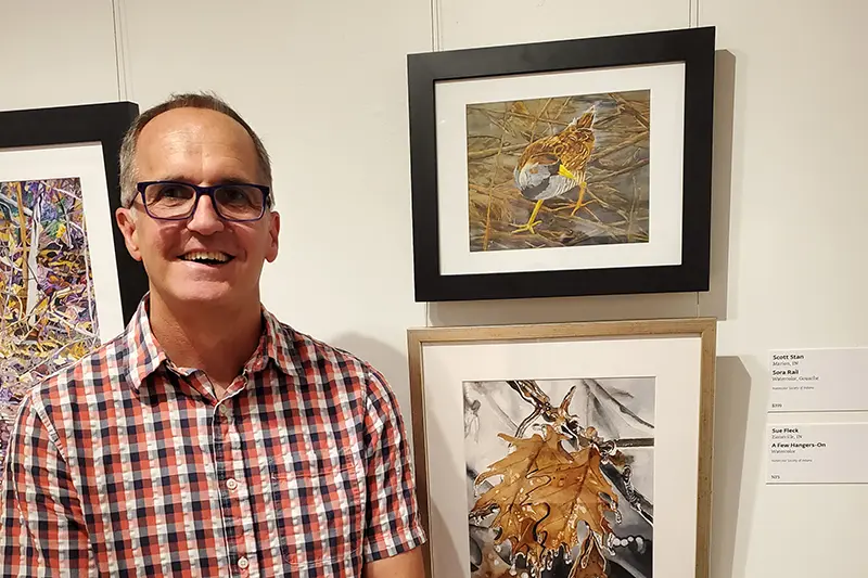 soccer coach Scott Stan standing next to watercolor paintings