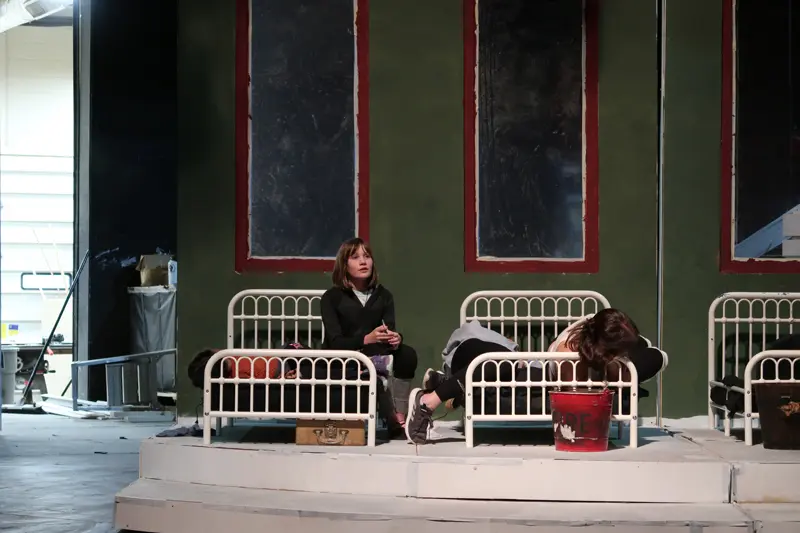 girl sits on metal frame bed on stage